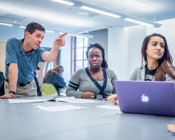 professor pointing at whiteboard while talking with students